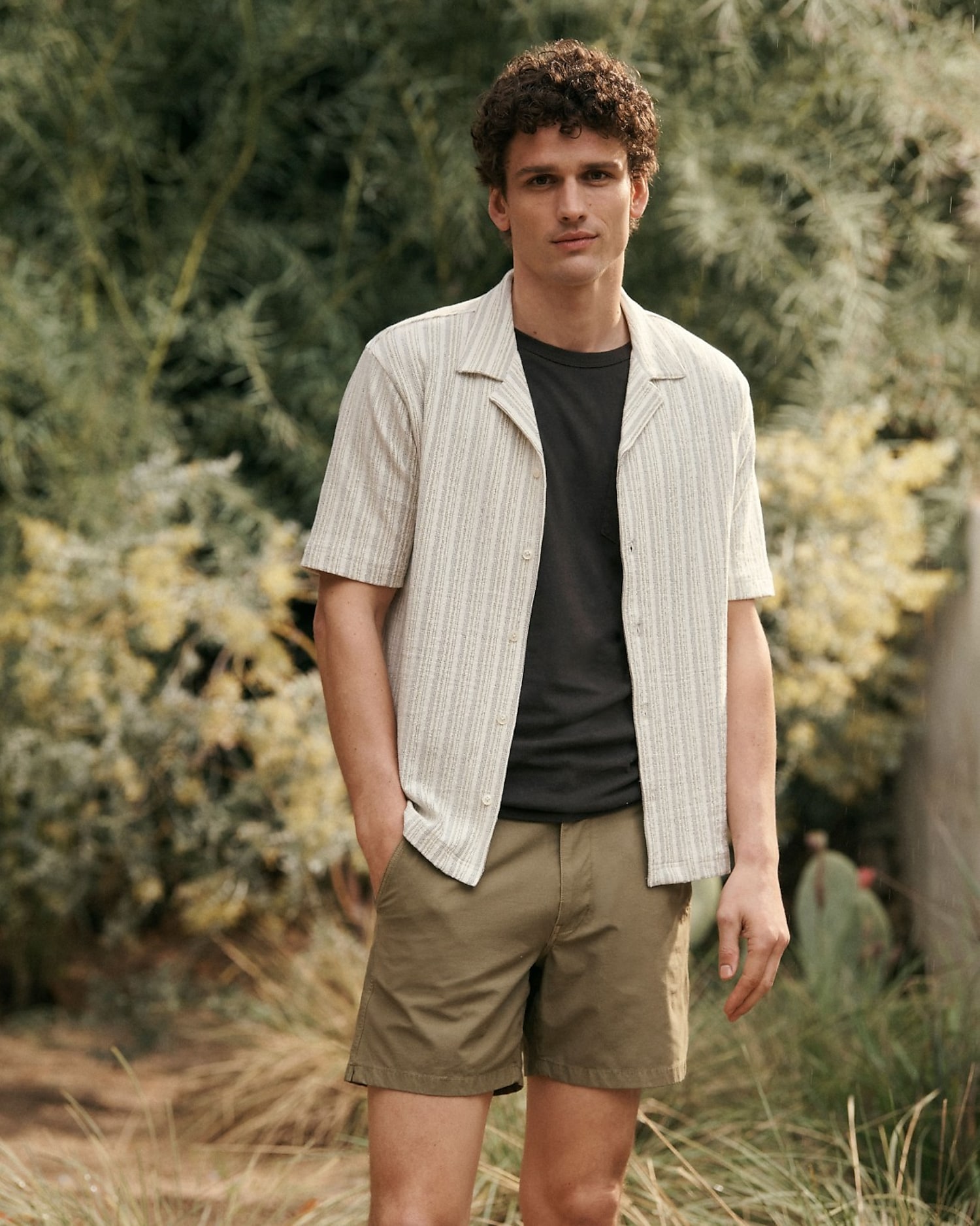 man standing in front of a parachute  with classic beige shorts, white top, and a beige shirt