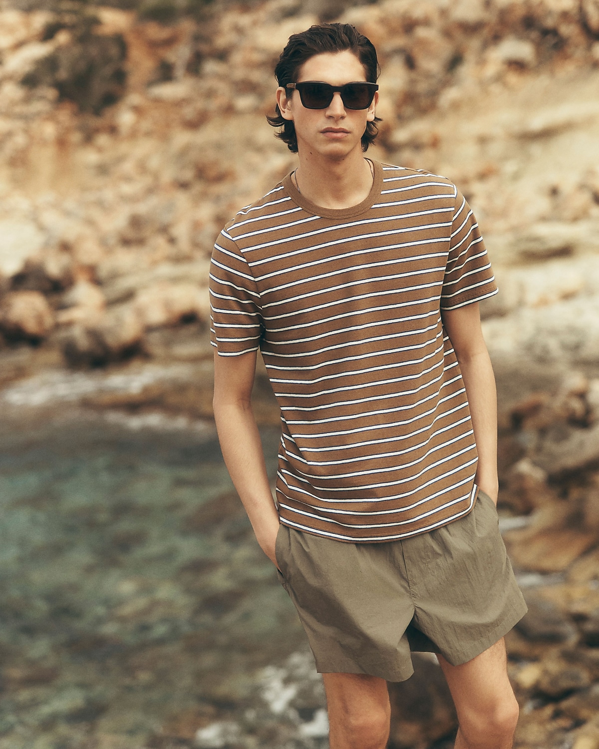 man standing in front of a parachute  with classic beige shorts, white top, and a beige shirt